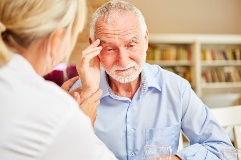 An older man touching his head in confusion while a doctor comforts him.