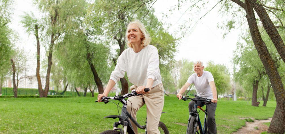 An elderly couple riding their bikes in the park.